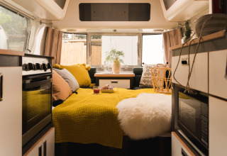 Moderne glamping-indkvartering i en PROCIDA Camp & Resort luxe airstream med hyggelig gul indretning.