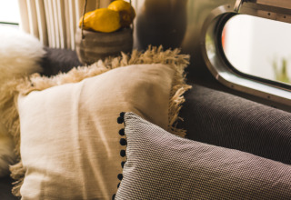 Cozy PROCIDA Camp & Resort airstream interior with soft cushions on a sofa near a large retro-style window.