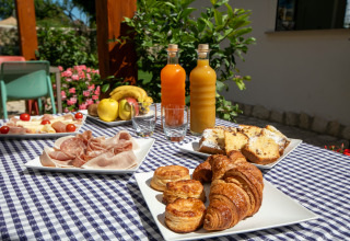 Frühstück im Freien bei Procida Camp & Resort mit Croissants, Kuchen, Aufschnitt, Obst und Säften.