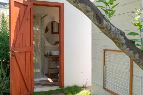 Porta in legno aperta su bagno moderno al PROCIDA Camp & Resort - Luxe airstreams, immerso nel verde.
