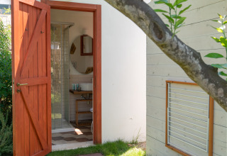 Puerta de madera abierta hacia un baño moderno en PROCIDA Camp & Resort - Luxe airstreams, rodeado de verde.
