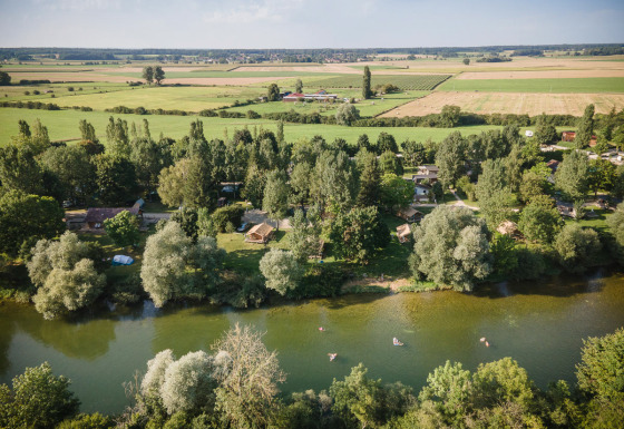 Luchtfoto van Huttopia La Plage Blanche - Glamping Franche-Comté met rivier, bomen en weilanden.