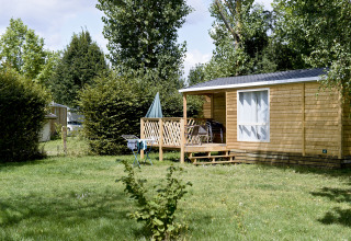 Cabaña de madera en Huttopia La Plage Blanche - Glamping Franche-Comté, rodeada de vegetación y árboles.