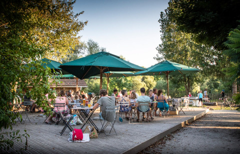 Zona de comedor exterior en Huttopia La Plage Blanche - Glamping Franche-Comté, con gente y sombrillas verdes.