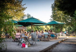 Zona de comedor exterior en Huttopia La Plage Blanche - Glamping Franche-Comté, con gente y sombrillas verdes.
