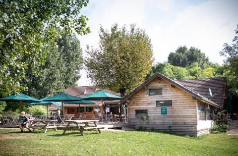 Area glamping di Huttopia La Plage Blanche in Franche-Comté con cabine di legno e ombrelloni verdi all’esterno.