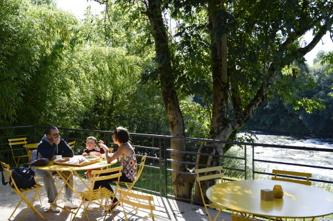 Family enjoys a meal at yellow outdoor tables by the river at Huttopia La Plage Blanche glamping site.