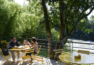Famille savourant un repas sur des tables jaunes au bord de la rivière à Huttopia La Plage Blanche glamping.
