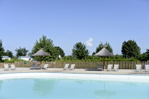 Outdoor pool with sun loungers and thatched umbrellas at Huttopia La Plage Blanche Glamping, Franche-Comté.
