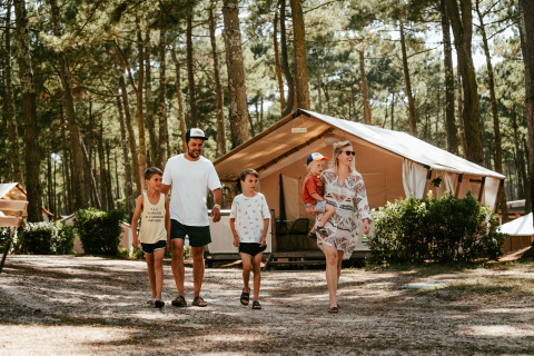 Familie går foran glamping lodge i skovområde ved Surf Tribe i Biscarrosse, Frankrig, under campingferie.
