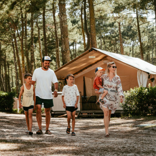 Familie går foran glamping lodge i skovområde ved Surf Tribe i Biscarrosse, Frankrig, under campingferie.