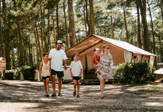 Une famille marche devant un lodge glamping à Surf Tribe à Biscarrosse, France, lors de vacances en camping.