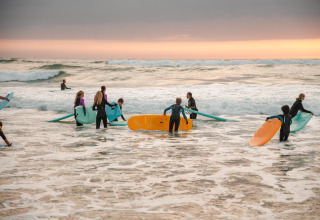 Children with surfboards at sunset, entering the water by Surf Tribe lodges in Biscarrosse, France.
