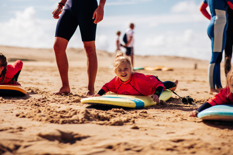 Children learning to surf at Biscarrosse beach with Surf Tribe camp, wearing wetsuits and using surfboards.