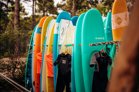 Surfbrætter og våddragter opstillet ved Surf Tribe i Biscarrosse, en glampingplads i Frankrigs natur.