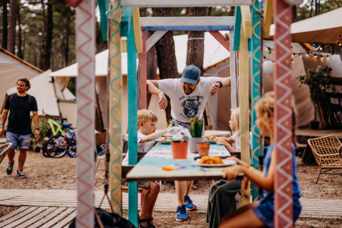 Familia comparte una comida al aire libre en coloridas mesas en Surf Tribe, glamping en Biscarrosse, Francia