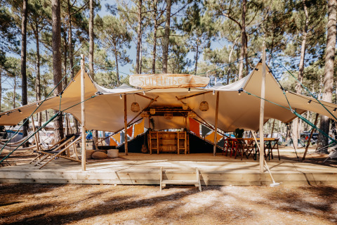 Glamping Surf Tribe in Biscarrosse, Frankrijk, luxe tent met houten terras te midden van dennenbomen.