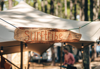 Pancarte en bois gravée 'Surftribe' devant un hébergement de glamping à Biscarrosse, France, nature autour.