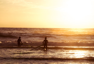 Dos surfistas entran al mar al atardecer junto a Surf Tribe en Biscarrosse, Francia, ideal para glamping.