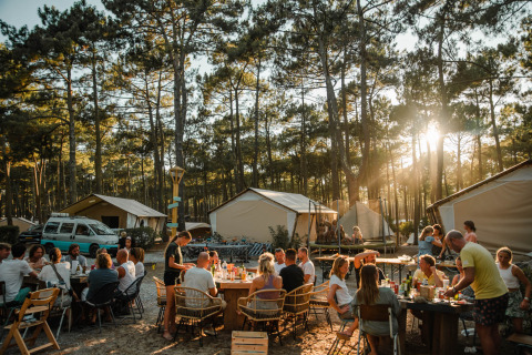 Hébergements glamping et groupes partageant un repas en forêt au Surf Tribe Biscarrosse, France