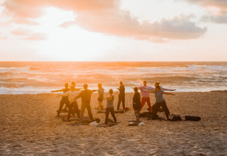 A group of people doing yoga on the beach at sunset near the sea at Surf Tribe in Biscarrosse, France.