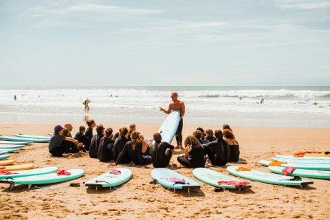 Surflessen op het strand bij Surf Tribe in Biscarrosse, Frankrijk, met een instructeur en groep deelnemers.