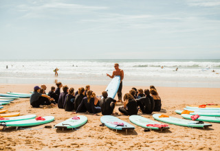 Surflessen op het strand bij Surf Tribe in Biscarrosse, Frankrijk, met een instructeur en groep deelnemers.