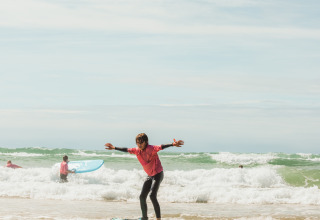 Kind surft op ondiep water bij Biscarrosse, andere surfers op de achtergrond, zonnige lucht en relaxte sfeer.