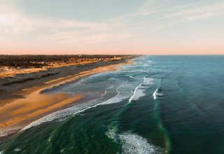 Aerial view of Surf Tribe in Biscarrosse, France, showing beach, waves, and glamping camps at sunset.