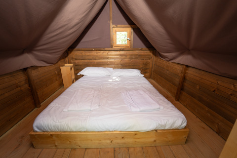 Cama acogedora y interior de madera en Vallicella Glamping Resort, experiencia de glamping en la Toscana.