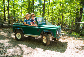 Due bambini guidano una mini jeep verde in un bosco soleggiato al Chianti Glamping Resort - Airlodges Toscane.