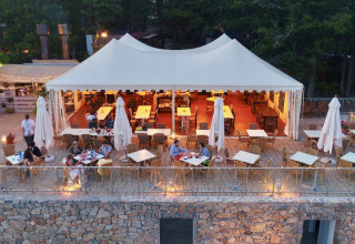 Terraza de restaurante en Chianti Glamping Resort con mesas bajo carpa y luces cálidas al atardecer.