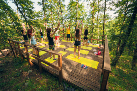 Groep mensen doet yoga op een houten platform in het bos bij Chianti Glamping Resort in Toscane.