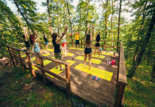 Gruppo che pratica yoga all'aperto su una terrazza di legno nella foresta al Chianti Glamping Resort in Toscana.