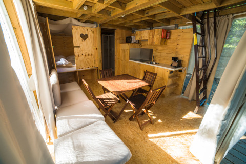 Interno di una luminosa tenda glamping con arredi in legno, cucina, tavolo da pranzo e scala al Chianti Glamping Resort.