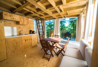 Inside a cozy wooden lodge at Chianti Glamping Resort, with kitchen, dining table, and forest view outside.