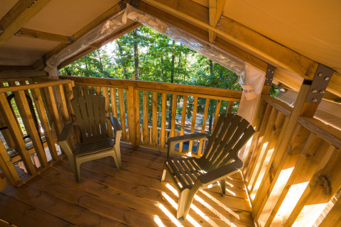 Houten terras met twee plastic stoelen bij Chianti Glamping Resort - Airlodges Toscane, omringd door bomen.