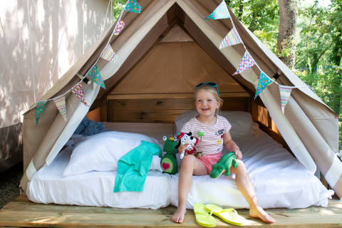 Un niño sonríe sentado en una cómoda tienda de glamping con banderines en Chianti Glamping Resort Toscana.
