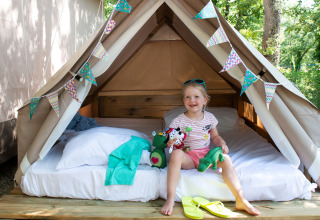 Ein Kind sitzt fröhlich in einem gemütlichen Glamping-Zelt mit bunter Girlande im Chianti Glamping Resort.