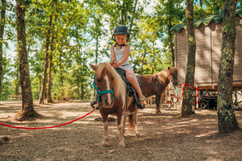 Bambina con casco monta un pony davanti a una casetta al Chianti Glamping Resort in Toscana in una giornata di sole.