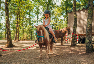 Kind met helm rijdt op een pony voor een houten hut bij Chianti Glamping Resort in zonnig Toscane.