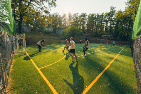 Young people play soccer on an artificial turf field surrounded by trees at Chianti Glamping Resort, Tuscany.