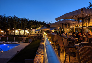 Evening dining at Chianti Glamping Resort in Tuscany, outdoor tables, guests, umbrellas and a lit swimming pool.