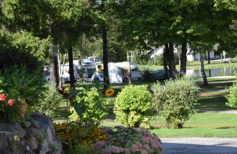 Camping Rosental Rož - Stacarvans Karinthië avec caravanes, végétation luxuriante, fleurs colorées et petit étang.