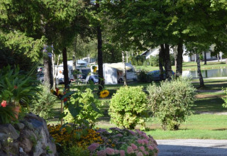 Camping Rosental Rož - Stacarvans Karinthië mit Wohnwagen, Bäumen, Blumenbeeten und Teich im Hintergrund.