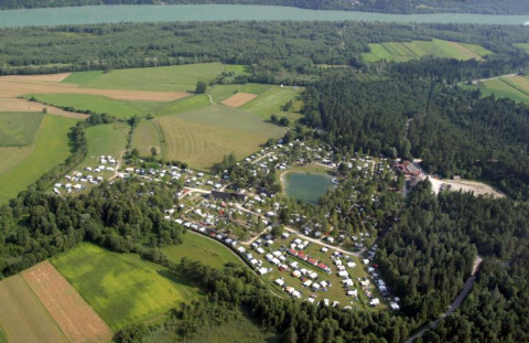 Luftfoto af Camping Rosental Rož - Stacaravans Karinthië, omgivet af skov og marker nær en sø.