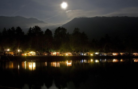 Nächtliche Ansicht vom Camping Rosental Rož, beleuchtete Glamping-Hütten am See unter Vollmond.