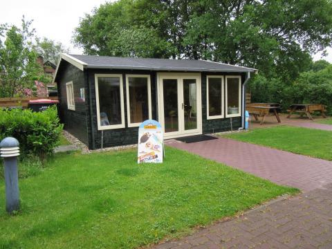 Zwarte houten hut bij Familiecamping Hendriks Wijkje - Safaritenten Drenthe omgeven door groen gras.