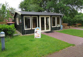 Cabaña de madera oscura en Familiecamping Hendriks Wijkje - Safaritenten Drenthe rodeada de césped verde.