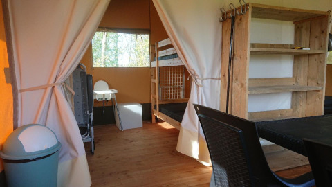 Vue intérieure d’une tente safari glamping avec lits superposés, étagère en bois, table et chaises.